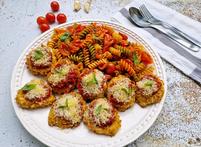 Plato de medallones de pavo a la parmesana acompañados de pasta.